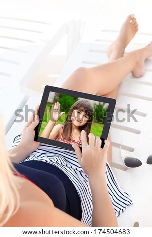 woman in a bathing suit lying on a chaise lounge with a computer tablet and communicates by video voice chat with a young child