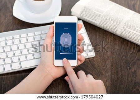 female hands holding a white touch phone over the desk in the office and entering the PIN code of fingerprint