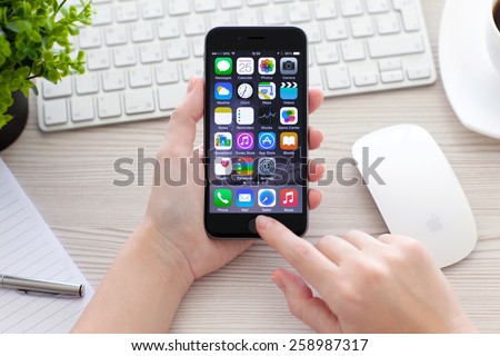 Alushta, Russia - October 25, 2014: Woman holding new phone iPhone 6 Space Gray over the table with iMac. iPhone 6 was created and developed by the Apple inc.