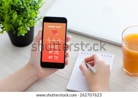 Women hands holding phone with app for health card monitoring and writing in a notebook