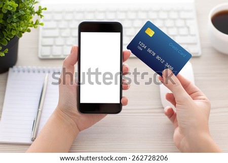 female hands holding phone with isolated screen and a credit card over the desk in the office