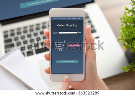 female hand holding white phone with online shopping on the screen on a table with a notebook