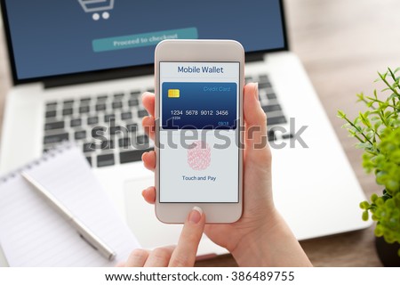 female hand holding a white phone with app mobile wallet on the screen on a table with laptop