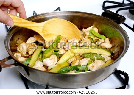 diced white chicken meat and fresh zucchini strips being sauteed in a frying pan
