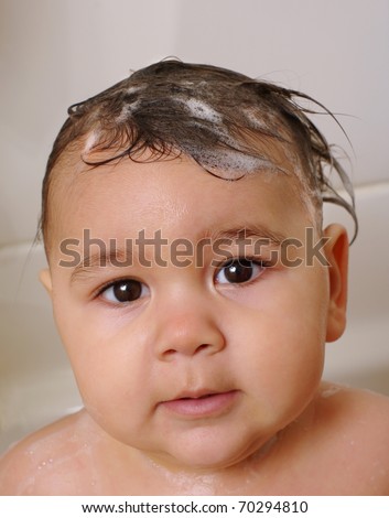Baby girl at bath-time, hair wet with shampoo suds, one year old