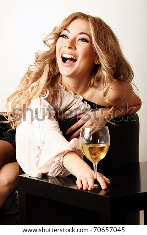 Laughing young beautiful young woman sitting on the chair with glass of white wine