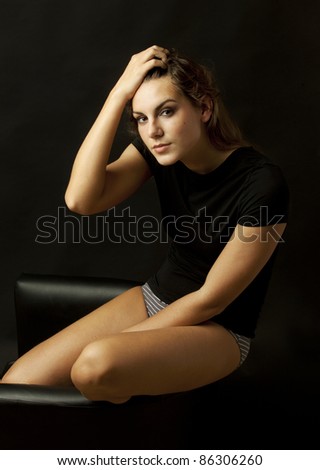 Young intelligent beautiful girl sitting on black chair on black background