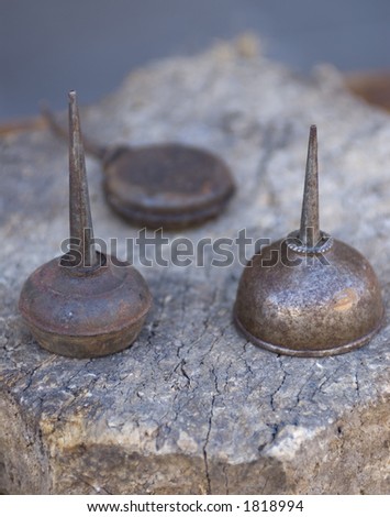 Three old rusted oil cans sit on top of a rustic looking piece of wood.