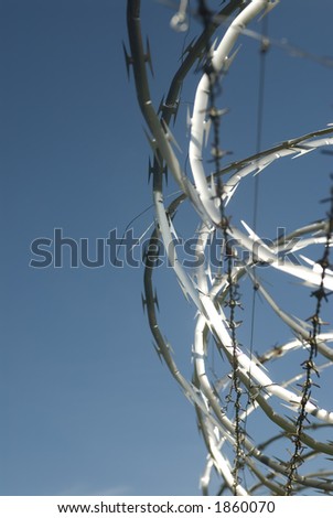 Razor wire runs along the top of a fence with a bright blue sky.
