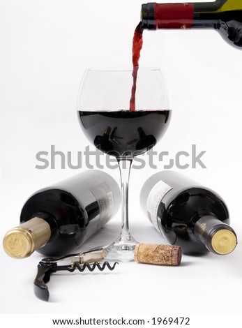 Pouring a glass of red wine with two bottles of unopened wine on the table.