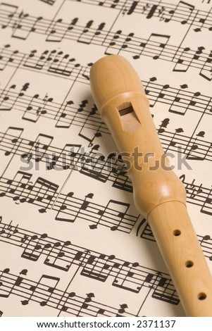 A simple wooden flute lies on top of a complicated musical score. Representing both the simplicity and complex nature of music