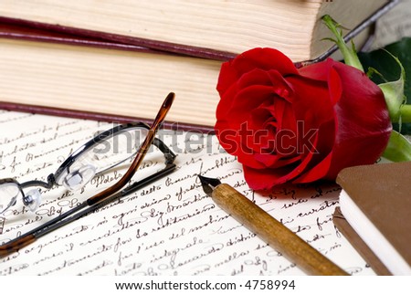 A red rose lays on top of a hand written document with a pile of books behind.