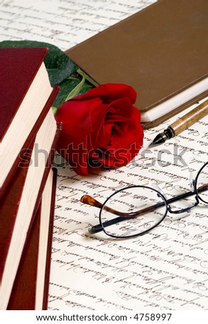 A red rose lays on top of a hand written document with a pile of books