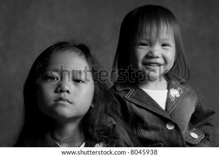 Two asian sisters, one with a smile and the other sad.