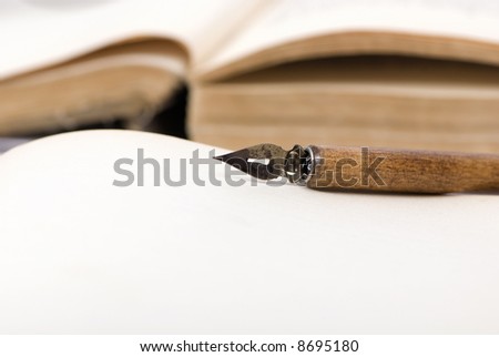 An old book that is open with a calligraphy pen on top.
