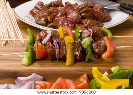 A plate full of fresh vegatables and meat for kabobs.