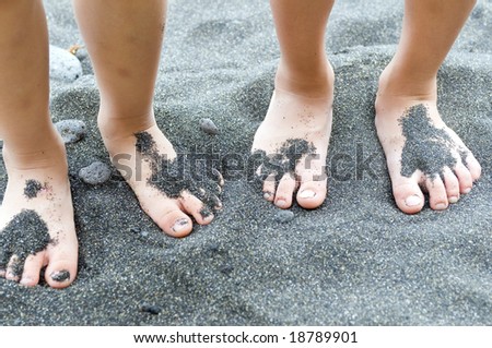 Two small sets of feet in black sand on the beach.