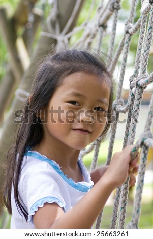 stock photo A young Asian Girl playing on a Rope ladder in a playground