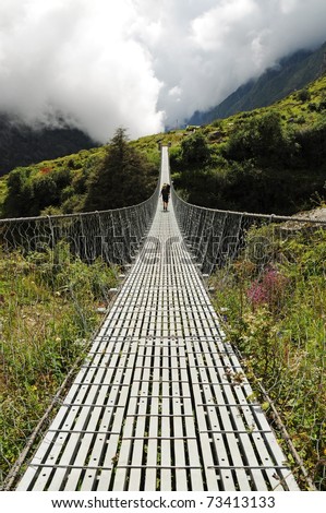 Long suspension foot bridge with silhouette of walking woman, bridge over deep valley in mountains, Himalaya, Nepal