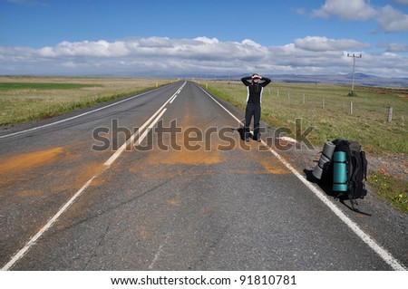 Young hitchhiking woman waiting for the ride (success) on the empty road