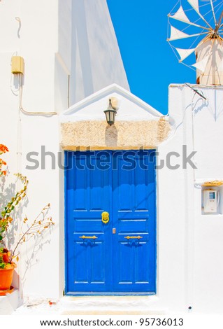 A wooden blue colored door of a Beautiful traditional house in Chora the capital of Amorgos island in Greece. A small windmill exists beside