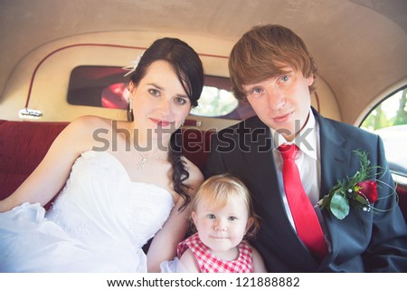 The bride and groom sit in the back seat of the limo with their daughter