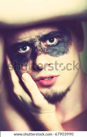 Emotive portrait of handsome man with black make up around his eyes and with hands covering part of his face. Low contrast