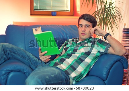 Portrait of an attractive young man with the book on couch in his living room