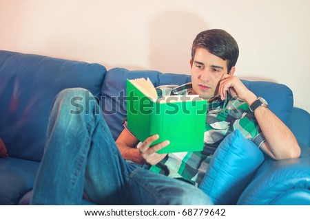 Portrait of an attractive young man with the book on couch in his living room over white background