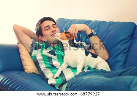 Portrait of an attractive young man playing with his cute dog lying on couch in his living room over white background
