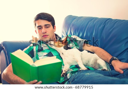 Portrait of an attractive young man with the book and his cute dog on couch in his living room over white background