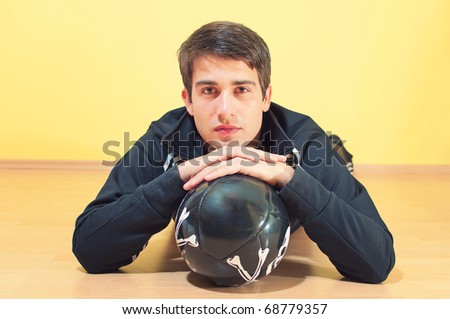 Portrait of a handsome young man lying on the floor in track suit holding a football on uniform background