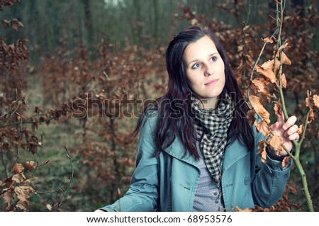 portrait of smiling beautiful young woman in the forest holding the tree and watching something