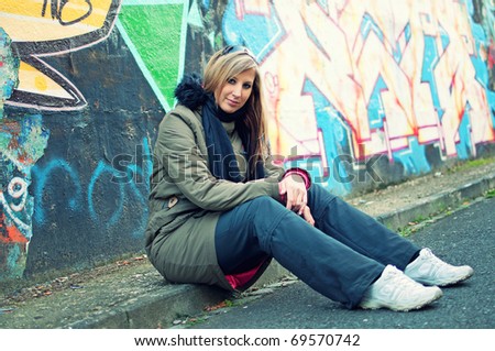 Beautiful young woman sitting by the road in front of graffiti wall