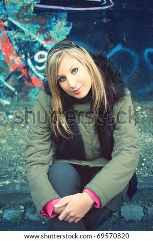closeup portrait of young woman sitting by the road in front of graffiti wall