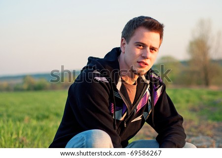 closeup portrait of handsome young man crouching on the grass in summer meadow
