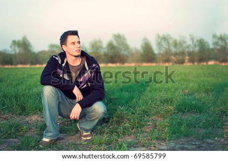 full length portrait of handsome young man crouching on the grass in summer meadow