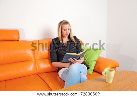 Attractive young lady reading an old book sitting on sofa