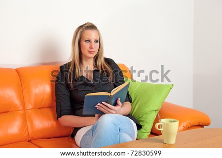 Attractive young woman reading an old book sitting on sofa