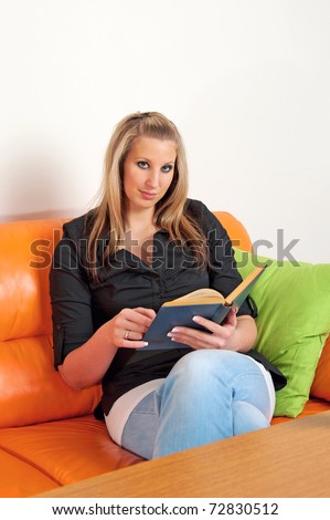 Beautiful young woman reading an old book sitting on sofa