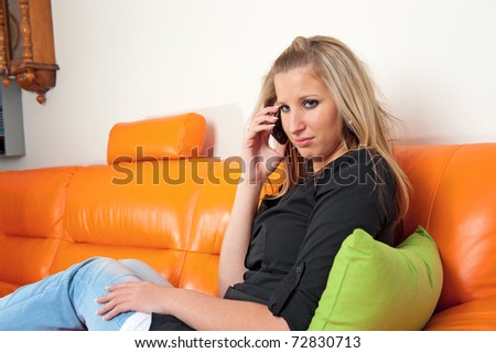Beautiful disappointed woman speaking on the phone and sitting on the sofa