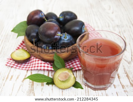 Glass with a Plum juice and fresh plums on a wooden background