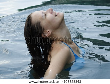 The beautiful young woman with long hair sits in the sea, having thrown back a head and have closed eyes, with a smile upon the face