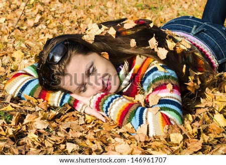 A beautiful young woman asleep lying on the yellow autumn leaves