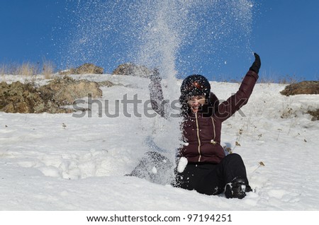 The beautiful young woman in mountain-skiing clothes has fun throwing upwards snow