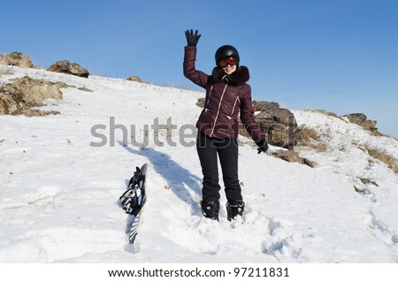 The beautiful young woman in mountain-skiing clothes, with a snowboard, costs on a grief and waves a hand