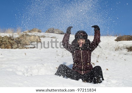 The beautiful young woman in mountain-skiing clothes has fun throwing upwards snow