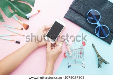 Top view of woman\'s using mobile phone for online shopping with beauty items on pastel color background, Online shopping