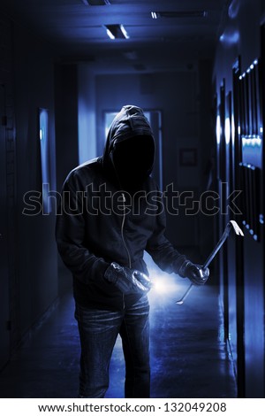 Burglar with flashlight and crow bar in a dark office building.