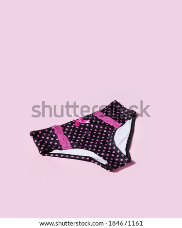 Women\'s black panties with pink polka dots on pink background with natural shadows.